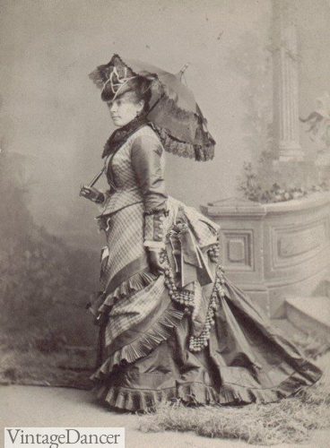 1876 dress - her large bustle reflects the earlier styles but the apron front is new