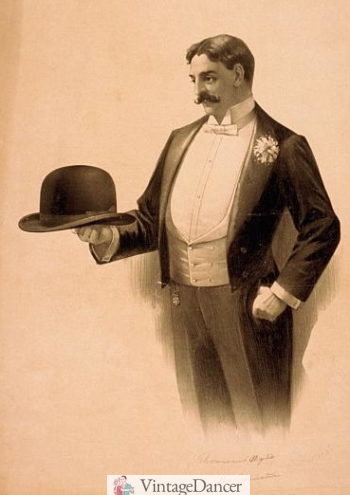 1896 tailcoat, white shawl vest, and white chrysanthemum boutonnière. Holding a derby hat. 