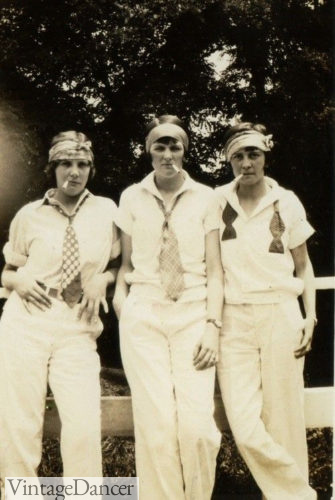 1920s women in pants. Playing tennis is men's white pants shirts neckties. The headscarves are the only women's item.