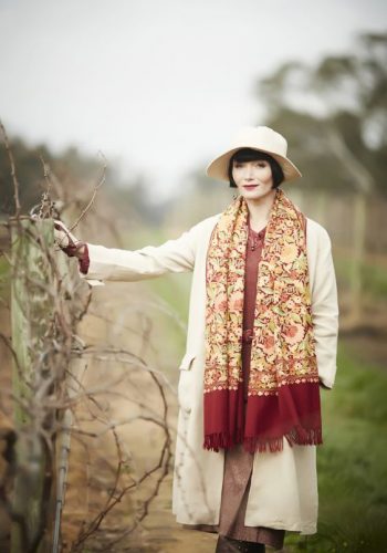 Miss Fisher wearing a wide fringe scarf casual hung from her neck