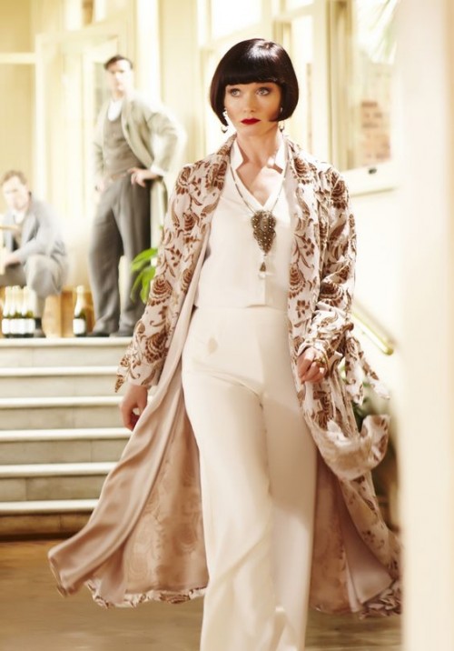 Miss Fisher wearing a white pant ensemble with kimono coat