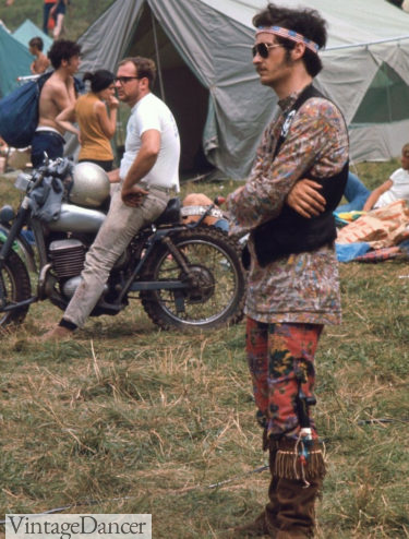 Woodstock man in American flag bandanna, tie dye shirt, patterned stockings, moccassin boots, and vest at VintageDancer